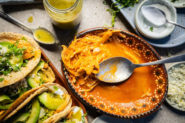 Plato de tinga junto a tacos de tinga con lechuga picada, salsa, crema, queso y aguacate