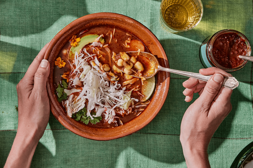 Bowl of pozole rojo topped with cabbage, avocado, cilantro, onions, and radishes