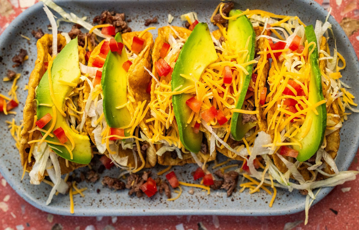 Crispy beef tacos topped with cheese, salsa, and avocado