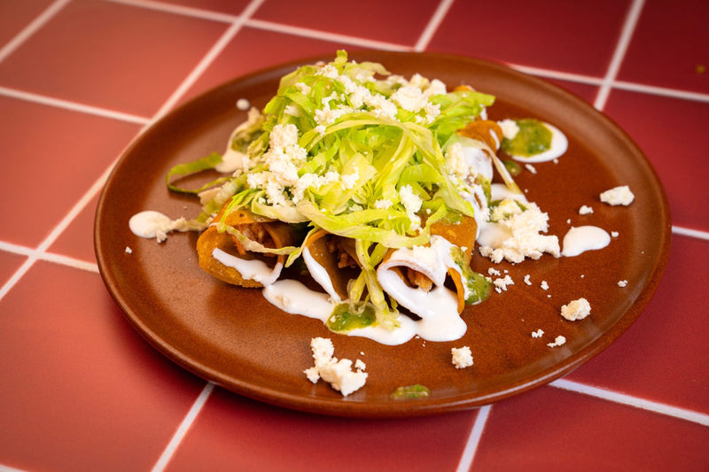 Flautas topped with lettuce, crema, and queso fresco